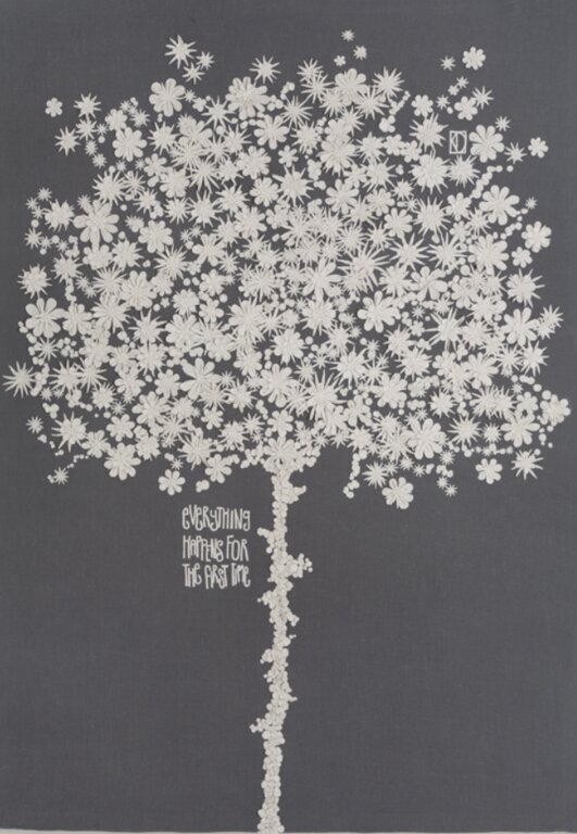  A piece of Kate's art. with a grey background with white flowers making the shape of a tree.  The words everything happens for the first time embroidered into the lower left quadrant.