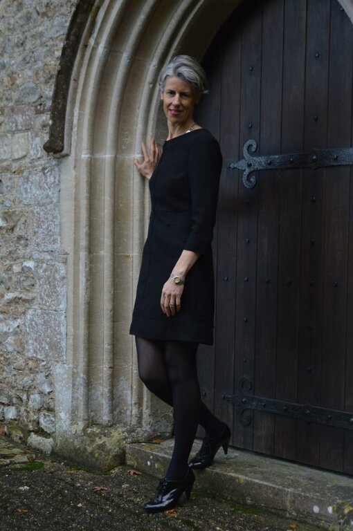  A photo of Samantha Knights standing against an old dark brown wooden arched door with heavy black iron hinges set in an old stone wall.